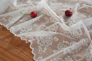 Detailansicht weißer Tischläufer aus Spitze mit Rosenmuster auf einer Holzoberfläche