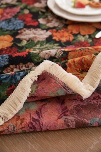 Makro-Detail der Retro-Jacquard-Tischdecke mit eleganten cremefarbenen Quasten auf Holz