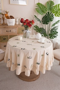Detail of cream round cotton tablecloth featuring embroidered panda and bamboo ruffles