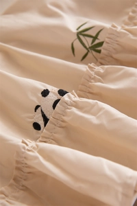 Detailed embroidery of a panda and bamboo leaves on apricot ruffled tablecloth fabric