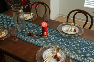 Dettaglio runner da tavola boho con trama geometrica blu e nappa su tavolo in legno scuro