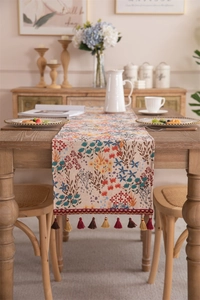 Close-up of floral jacquard table runner with decorative tassel trim on wooden table