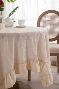 Close-up of French floral embroidery and elegant ruffle edge on cream cotton tablecloth