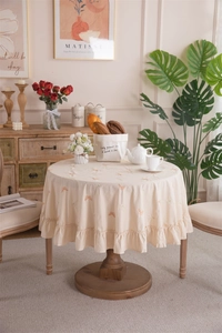 Detail of round beige cotton tablecloth with orange butterfly embroidery and ruffled edge