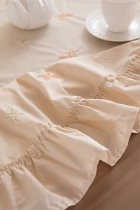 Detail of apricot cotton tablecloth featuring floral embroidery and ruffle edges