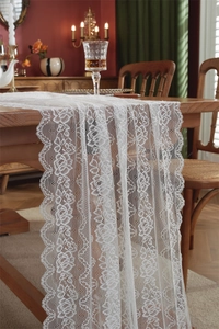 Detail eines weißen französischen Tischläufers aus Spitze mit Rosenmuster auf Holztisch