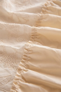 Detailed embroidery and ruffled edging on a cream cotton French-style tablecloth