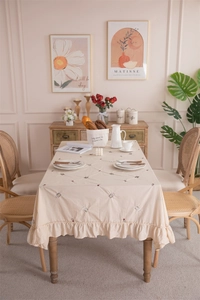 Macro detail of beige cotton tablecloth featuring floral embroidery and elegant ruffled edges