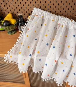 Detail of white cotton cafe curtain with colorful polka dots and white pom-pom trim edge