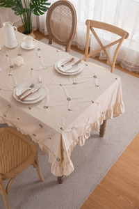 Detail of cream cotton tablecloth featuring animal embroidery and ruffled frill edges