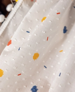Macro detail of cotton fabric with colorful patterns and white pom-pom lace trim
