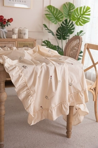 Detailed embroidery of a small owl on a beige ruffled cotton tablecloth for round tables