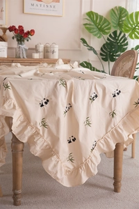 Detail of ruffled edge beige cotton tablecloth featuring panda and bamboo embroidery