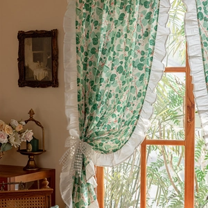 Detail of floral cotton curtain with green leaf print, ruffle edges and a lace bow tie-back