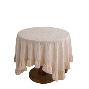 Round cream white embroidered tablecloth with ruffled edges on a wooden side table