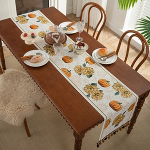 Polyester table runner featuring pumpkins and sunflowers with tassels on a wooden table