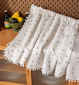 Detail view of cotton cabinet curtain with red floral pattern and white pom-pom trim