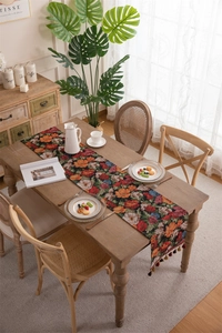 Detail of vintage floral jacquard table runner with dark tassels on wooden dining table