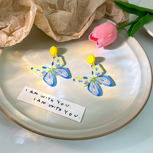 Detailed close-up of blue and yellow floral butterfly earrings on a ceramic dish
