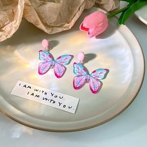 Close-up of butterfly earrings with pink and blue gradient wings on a white plate