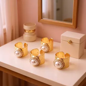 Detail of four gold hammered rings with large white pearls and crystal halo on a beige table