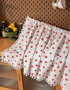 Detail of cotton curtain with red strawberry prints and decorative white pom-poms