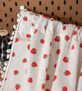 Close-up of white cotton curtain with red strawberry print and soft pom-pom fringe