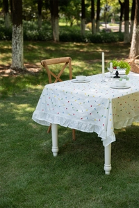 Detail of white cotton tablecloth with colorful geometric dots and ruffled edge design