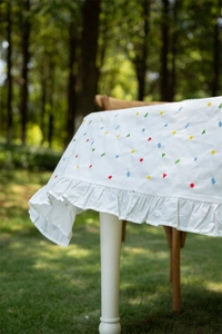 Detail of white cotton tablecloth with colorful geometric embroidery and ruffle edges