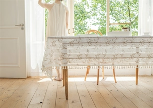 Detail der beigen Jacquard-Tischdecke mit braunem Muster und Quastensaum auf Holztisch