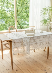 Detail der cremefarbenen Jacquard-Tischdecke mit goldenem Blumenmuster und Quastensaum