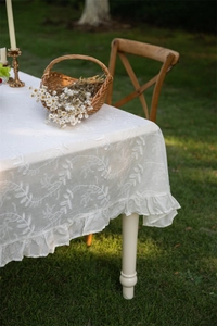 Detail of white cotton lace tablecloth with floral embroidery and ruffle edges in garden