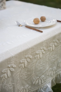 Detailed embroidery of leaf patterns on white cotton tablecloth with ruffled edges
