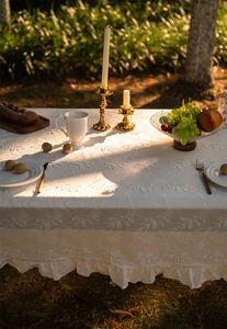 Detailed embroidery of leaf patterns on cream lace tablecloth with elegant ruffled edges