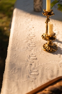 Detail of white cotton lace tablecloth with leaf embroidery and ruffled edge in sunlight