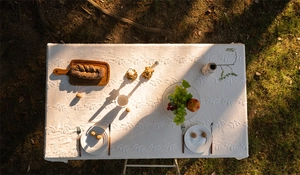 Detail of white cotton tablecloth with 3D leaf embroidery on grass at sunset