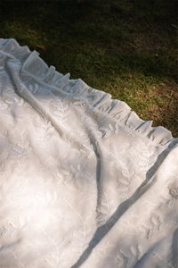 Detail of white cotton lace tablecloth showing leaf embroidery and ruffled edge on grass