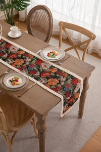 Close-up of vintage floral jacquard table runner with white tassels on a wooden table