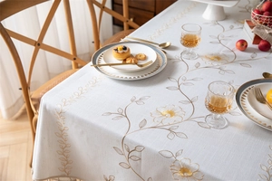 Close-up of elegant white floral embroidery with gold threads and tassel edge on tablecloth