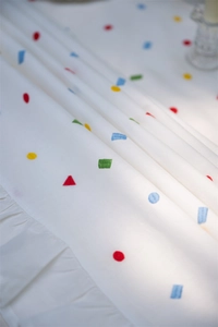 Close-up of white cotton tablecloth featuring colorful geometric embroidery and ruffled edges
