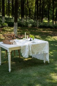 Detail of white cotton tablecloth with geometric embroidery and ruffled hem in nature