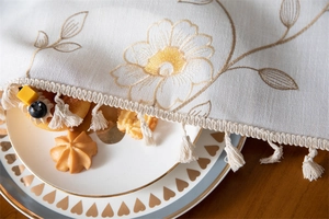 Detail of embroidered coffee leaf pattern on beige tablecloth with elegant white tassels