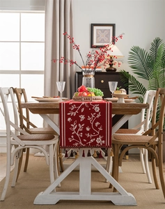Detail of red festive table runner with white floral embroidery and tassel fringe