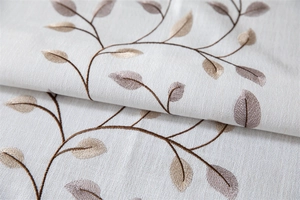 Detail of embroidered vine leaves on linen-textured beige tablecloth fabric