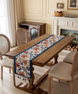 Detail of vintage floral table runner with blue tassels on a dark wooden table