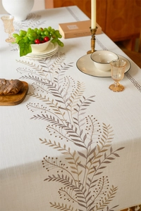Detail of coffee leaf embroidery and tassel edge on a beige cotton linen tablecloth