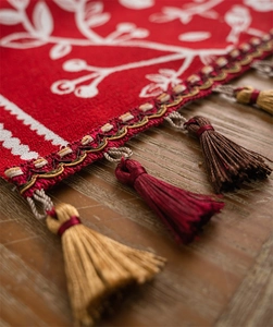 Detail of red festive table runner showing white floral embroidery and colorful tassels