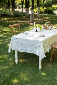Detailed close-up of French cotton tablecloth featuring multi-color floral embroidery and ruffles