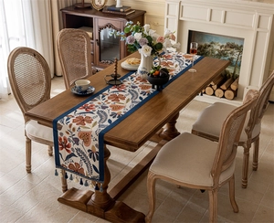 Close-up of vintage floral table runner with blue fringe tassels on a wooden dining table