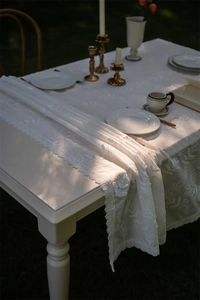 Close-up of white lace table runner with leaf embroidery and wavy lace edges on wooden table